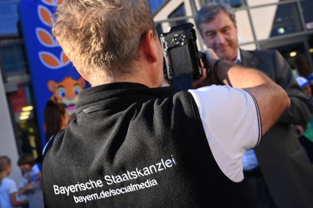 Der Ruecken einer Person mit dem Schriftzug Bayerische Staatskanzlei ,Social Media im Vordergrund eines Schultermins mit Ministerpraesident Markus Soeder. Markus SOEDER (Ministerpraesident Bayern und CSU Vorsitzender) besucht gemeinsam mit Gesundheitsministerin Judith Gerlach und Kultusministerin Anna Stolz am 06.10.2026 die Sport-Grundschule an der Margarethe-Danzi-Straße in Muenchen und informiert sich im Vorfeld des landesweiten Praeventionstages am 12. Oktober über erfolgreiche Praevention und Gesundheitsfoerderung im Schulalltag