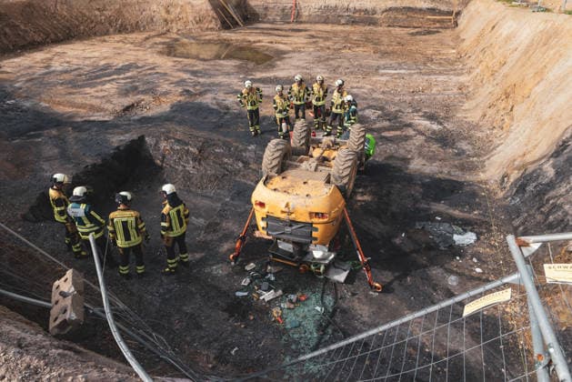RECORD DATE NOT STATED Feuerwehr und Rettungsdienst versorgen eine Person neben einem umgestürzten Radlader in einer Baugrube an der Charlottenstraße in Bochum-Wiemelhausen. Die Baumaschine war etwa dreieinhalb bis vier Meter tief abgestürzt und auf dem Dach liegen geblieben. Einsatzkräfte sichern das Fahrzeug mit Stützen.