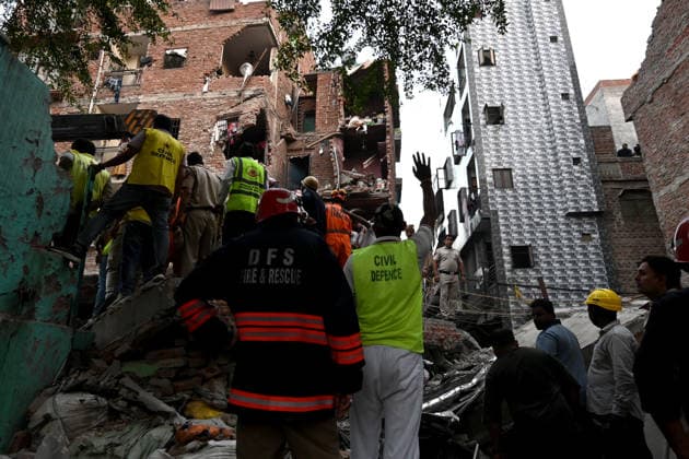 NEW DELHI, INDIA - OCTOBER 7: National Disaster Response Force (NDRF) jawans, Delhi Fire Service personnel, and local residents navigate heavy rubble during a search and rescue operation after a four-storey residential building collapsed in the New Seemapuri area of Shahdara on October 7, 2026, in New Delhi, India. The structural collapse occurred around 3:30 PM behind the local fish market, trapping multiple residents under concrete slabs and damaging two adjoining houses. At least one minor died while eight people were rescued and rushed to Rajiv Gandhi Super Speciality Hospital for emergency medical treatment as sniffer dogs and excavators worked late into the evening to locate remaining trapped survivors. (Photo by Ishant Chauhan Hindus