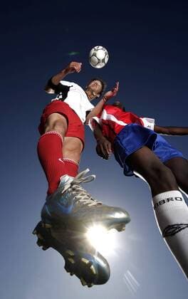 Fußballspieler im Kopfballduell unter Sonnenschein - MODEL RELEASED Fußball Herren Freizeitfußball 2005, Symbol, Feature, Aufmacher, Freizeitsport, Freizeitsportler Gruppe Froschperspektive, unten, Zweikampf, Duell Dynamik, Höhe,