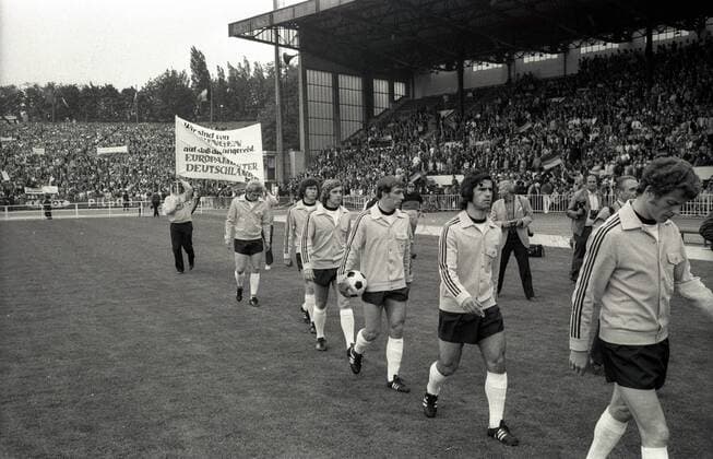 Einmarsch BR Deutschland v.re.: Herbert Wimmer, Gerd Müller, Horst Dieter Höttges, Erwin Kremers, Paul Breitner und Uli Hoeneß; dahinter zwei deutsche Fans mit ihrem Plakat: Wir sind von Bingen angereist, auf daß der Europameister Deutschland heißt Fußball Länderspiel Herren EM 1972, Nationalmannschaft, BRD, Finale Endspiel Vneg Vsw Totale Heyselstadion Heysel Stadion Brüssel Fußball Länderspiel Herren EM 1972, Nationalmannschaft, BRD, Finale Endspiel Vneg Vsw Totale Heyselstadion Heysel Stadion Brüssel