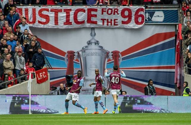 Christian Benteke of Aston Villa celebrates his goal with Fabian Delph and Jack Grealish of Aston Villa in front of the Liverpool fans and the Justice for the 96 banner during the The FA Cup Semi-Final match between Aston Villa and Liverpool at Wembley Stadium, London, England on 19 April 2015. Copyright: xLiamxMcAvoyx 03950092