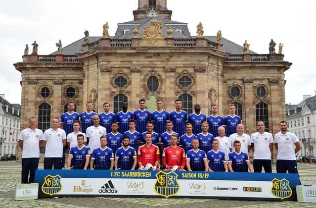 Das Team des 1. FC Saarbrücken am Donnerstag (12.07.2018) vor der Ludwigskirche in Saarbrücken. Im Bild: Obere Reihe (v.l.) Marco Holz ( 14), Macel Carl ( 22), Steven Zellner ( 5), Alexandre Mendy ( 4), Benjamin Kessel ( 15), Oliver Oschkenat ( 3), Nino Miotke ( 28), Jose Pierre Vunguidica ( 9), Sebastian Jacob ( 24) und Marco Kehl-Gomez. Mittlere Reihe: (v.l.) Robert Roelofsen (Co-Trainer), Dirk Lottner (Cheftrainer), Christoph Fuhr (Athletiktrainer), Heinz Böhmann (Torwart-Trainer), Gillian Jurcher ( 21), Lukas Quirin ( 31), Markus Obernosterer ( 10), Manuel Zeitz ( 8), Tobias Jänicke ( 25), Pierre Fassnacht ( 29), Helmut Schwan (Betreuer), Rüdiger Schmid (Zeugwart), Paulo da Palma (Physiotherapeut) und Frank Kackert (Torwart-Trainer). Untere Reihe: (v.l.) Fatih Köksal ( 27), Sascha Wenninger ( 19), Fanol Perdedaj ( 17), Ricco Cymer ( 20), Daniel Batz ( 1), Martin Dausch ( 7), Markus Mendler ( 11) und Mario Müller ( 23).