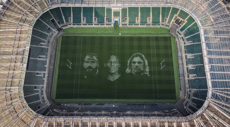 The pitch at Twickenham Stadium has been transformed into a stunning portrait featuring three of Premiership Rugby?s star players today (12th August 2020). The giant rugby art, the largest outdoor painting ever created in the UK, was unveiled to celebrate the restart of Gallagher Premiership Rugby on Friday 14 th August when Harlequins take on Sale Sharks at 7:45pm, just 200 metres away. The artwork features Harlequins player, Joe Marler; Saracens? Maro Itoje, as well as Sale Sharks? Rugby World Cup winner Faf de Klerk. It took team of eight artists more than 24 hours to complete the pitch portrait and more than 100 hours of planning before any paint touched the grass. A bespoke computer program was written to generate the precise measurements that were needed to create the artwork to the exact scale of the stadium. The image, which occupies most of the 7,000 square metre pitch, was created using a grid comprised of 13,420 elements. Each painted line in the portrait is just 6 inches wide. Nearly 1280 litres of biodegradable pitch marker paint were used for the elaborate creation. An estimated 150,000 passengers will enjoy the spectacle from the sky this week on flights in and out of London?s Heathrow airport. Faf de Klerk was one of the featured Premiership Rugby stars in the portrait. The Sale Sharks star said, I didn t realise it was going to be on the field, I thought it was going to be a photo up somewhere or on the big screen. It s looking really cool. There are a lot of great players in the Premiership, and it is amazing. I feel really privileged and quite humble . Speaking about the impact of lockdown on the Saracens star Maro Itoje said The last few months have been really tough on fans and players but we?re back and we?re ready for the start of the season on Friday 14th August. The past five months has shown us how important the sport is and what it brings to people lives. British artist John Lundberg, who oversaw the po Copyright: xScottxGarfitt PinPep CoverxImagesx 0103040074st EDITORIAL USE ONLY. RESTRICTED TO NEWSPAPERS BASED IN THE UK