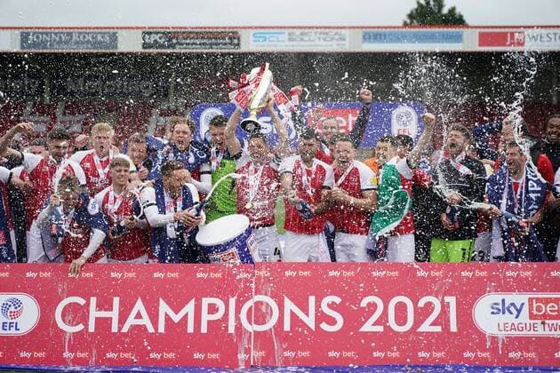 Mandatory Credit: Photo by Jed Leicester BPI Shutterstock (11893253dd) Cheltenham Town captain Ben Tozer lifts the EFL Sky Bet League Two championship trophy as the rest of his team mates celebrate together with the victory champagne Cheltenham Town v Harrogate Town, EFL Sky Bet League Two, Football, The Jonny-Rocks Stadium, Cheltenham, UK - 08 May 2021 EDITORIAL USE ONLY No use with unauthorised audio, video, data, fixture lists, club league logos or live services. Online in-match use limited to 120 images, no video emulation. No use in betting, games or single club league player publications. Cheltenham Town v Harrogate Town, EFL Sky Bet League Two, Football, The Jonny-Rocks Stadium, Cheltenham, UK - 08 May 2021 EDITORIAL USE ONLY No use with unauthorised audio, video, data, fixture lists, club league logos or live services. Online in-match use limited to 120 images, no video emulation. No use in betting, games or single club league player publications. Copyright: xJedxLeicester BPI Shutterstockx 11893253dd