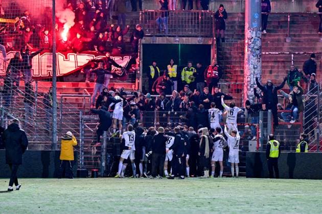 Nach dem gewonnenen Elfmeterschiessen gab es für die Spieler des SV Wacker Burghausen kein Halten mehr, sie stuermten zu den mitgereisten Fans und feierten den Einzug ins Halbfinale, Freude, freundlich, frohlich, strahlend, optimistisch, 18.11.2025, Unterhaching (Deutschland), Fussball, BFV Verbandspokal, Viertelfinale, SpVgg Unterhaching - SV Wacker Burghausen