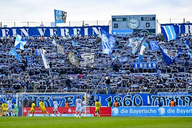 Fans des TSV 1860 Muenchen zeigen ihre Schals, schwenken Fahnen und machen Stimmung, Fans, Publikum, Zuschauer, Stimmung, Atmosphaere, Stadion, 23.11.2025, München (Deutschland), Fussball, 3. Liga, TSV 1860 München - 1. FC Saarbrücken, DFB DFL REGULATIONS PROHIBIT ANY USE OF PHOTOGRAPHS AS IMAGE SEQUENCES AND OR QUASI-VIDEO.