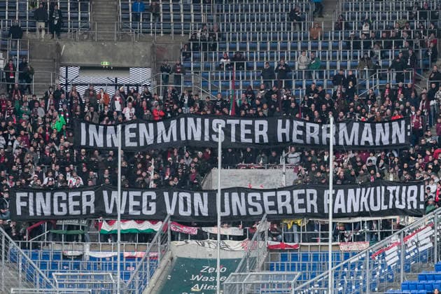 Die Fans vom FC Augsburg zeigen in der Fankurve ein Banner, Spruchband mit der Aufschrift: Innenminister Herrmann - Finger weg von unserer Fankultur, Fans, Ultras Publikum, Zuschauer, Stimmung, Atmosphäre, Stadion, Protest, Protestaktion gegen Staatsminister Joachim Herrmann (nicht im Bild), den Bayerischen Innenminister, der im Dezember an der Innenministerkonferenz (IMK) teilnehmen wird, bei der umfassende Sicherheitsmaßnahmen für Fußballspiele beschlossen werden könnten, protestieren, Aktion, Action, 29.11.2025, Sinsheim (Deutschland), Fussball, Bundesliga, TSG 1899 Hoffenheim - FC Augsburg, DFB DFL REGULATIONS PROHIBIT ANY USE OF PHOTOGRAPHS AS IMAGE SEQUENCES AND OR QUASI-VIDEO.