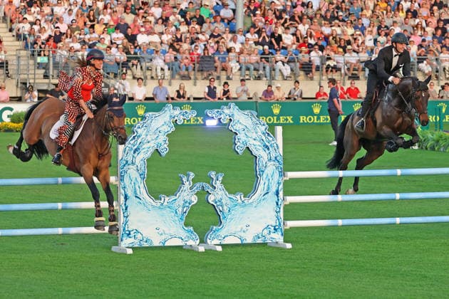 Richard Vogel und Luciana Diniz im Tempo gemeinsam in Bond-Stunt-Feeling über die Hindernisse, Konzert Pferd & Sinfonie, Rahmenprogramm, Motto des Abends: James Bond, Weltfest des Pferdesports, World Equestrian Festival, TSCHIO Aachen 2026, TSCHIO statt CHIO 2026, Aachener Soers, 22. bis 24. Mai 2026, Reitsport, 23.05.2026, Aachen Aachener Soers Deutschland