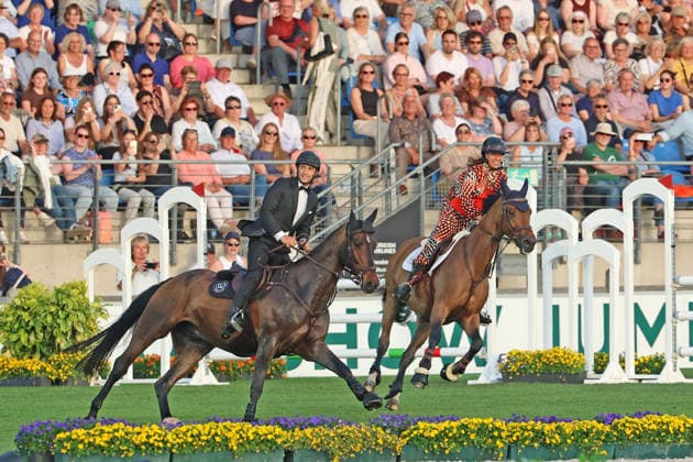 Richard Vogel und Luciana Diniz im Tempo gemeinsam in Bond-Stunt-Feeling über die Hindernisse, Konzert Pferd & Sinfonie, Rahmenprogramm, Motto des Abends: James Bond, Weltfest des Pferdesports, World Equestrian Festival, TSCHIO Aachen 2026, TSCHIO statt CHIO 2026, Aachener Soers, 22. bis 24. Mai 2026, Reitsport, 23.05.2026, Aachen Aachener Soers Deutschland