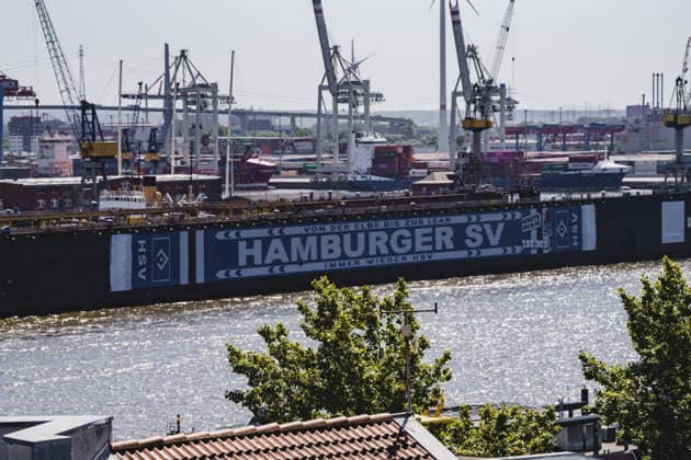 Deutschland, Hamburg, Hamburger Hafen, Blohm+Voss Dock 11, Dock 11, Schwimmdock, Hamburger SV, HSV, HSV Werbung, Mitgliederwerbung, HSV Banner, HSV Schal, Fußballkultur, Traditionsverein, Aufstiegskampagne, Raute-Dich.de, Von der Elbe bis zur Isar immer wieder HSV, Hafen Hamburg, Elbe, Hafenkräne, Containerterminal, Werft, Werftindustrie, Schiffswerft, Dockanlage, maritime Szene, Industriehafen, Hafenpanorama, Hafenbetrieb, Schifffahrt, Wasserverkehr, Containerhafen, Hafenfotografie, maritime Fotografie, Urban Photography, Norddeutschland, Stadtansicht, Industriearchitektur, Docklands, Elbansicht, Morgenlicht, Sonnenlicht, Sommerlicht, Hamburger Skyline, Hafenindustrie, Großwerft, Bannerwerbung, Outdoor Werbung, Logistik, Containerlogistik, Windkraftanlagen Copyright: xStefanxTrochax