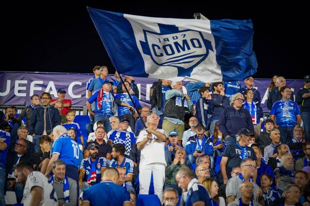 Italien: Fussball UEFA Champions League 2026 - 2027, 1. Spieltag - Como 1907 vs RB Leipzig - Giuseppe Sinigaglia (Como): Fans und Anhänger von Como 1907 auf der Tribüne im Stadion Giuseppe Sinigaglia schwenken eine große blau-weiße Vereinsfahne mit Como-1907-Logo. Fußball, Champions League, Como 1907, Zuschauer, Fans, Tribüne, Fanblock, Fankultur, Fahne, Flagge, Vereinswappen, Vereinsfarben, Stimmung, Heimfans, Italien. Copyright: xJOERANxSTEINSIEKx