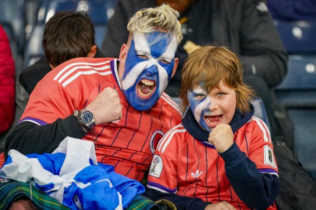 Fussball UEFA Nations League 2026 - 2027, 2. Spieltag - Schottland vs Schweiz - Hampden Park (Glasgow): Schottische Fans im Hampden Park beim Spiel Schottland gegen Schweiz. Ein Mann und ein Junge tragen Schottland-Trikots und haben ihre Gesichter in den Farben der schottischen Flagge bemalt. Beide jubeln mit geballter Faust. Fussball, UEFA Nations League, Schottland, Schweiz, Fans, Zuschauer, Fankultur, Vater und Sohn, Gesichtsbemalung, Saltire, Schottland-Fahne, Jubel, Emotionen, Tribüne, Hampden Park, Glasgow. Copyright: xJOERANxSTEINSIEKx