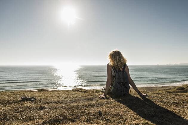 Back view of teenage girl sitting on the beach at evening twilight looking to the sea model released Symbolfoto UUF08740