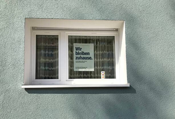 27.03.2020, Berlin, GER - Wir bleiben zuhause-Plakat haengt im Fenster eines Wohnhauses. (Alltag, Ausgangsbeschraenkung, Ausgangssperre, aussen, Aussenaufnahme, Berlin, Coronaepidemie, Coronainfektion, Coronapandemie, Coronavirus, Coronavirus SARS-CoV-2, Covid 19, Covid-19, deutsch, Deutschland, Europa, europaeisch, Fassade, Fenster, Fruehjahr, Fruehling, Gesellschaft, Haus, Jahreszeit, Kontakt vermeiden, Kontaktverbot, Mehrfamilienhaus, Mietshaus, niemand, Plakat, QF, Querformat, Shutdown, Stadt, Stadtansicht, Stadtbild, Stadtleben, Statement, Westeuropa, Wir bleiben zuhause, Wohnhaus) 200327D803BERLIN.JPG
