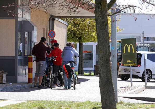 18.04.2020, Mahlow, Brandenburg, GER - Fahrradfahrer stehen am Abholschalter eines Drive-in von McDonalds. (abholen, Abholschalter, Abholung, Alltag, aussen, Aussenaufnahme, bestellen, Bestellschalter, Bestellung, Brandenburg, deutsch, Deutschland, Drive-in, Ernaehrung, Essen, Europa, europaeisch, Fahrradfahrer, Fast Food, Fast-Food, Fastfood, Fastfood Kette, Fastfood Restaurant, Fastfood-Kette, Fastfood-Restaurant, Fastfoodkette, Fastfoodrestaurant, Filiale, Freizeit, Gastronomie, Gesellschaft, Gruppe, Humor, Kaukasier, kaukasisch, lustig, Mahlow, Mc Donalds, Mc Donalds-Filiale, McDonalds, Menschen, Mittagessen, Mittagspause, Mittagszeit, Pause, Personen, QF, Querformat, Restaurant, Schnellimbiss, warten, Wartezeit, Wirtschaft, Witz, witzi