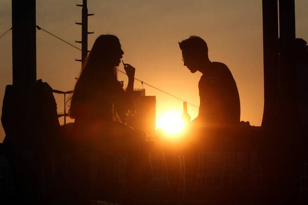 Ein Paar sitzt im Gegenlicht der untergehenden Sonne auf einem Träger der Hackerbrücke in München und unterhält sich, Bayern, Deutschland.