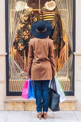 Back view of unrecognizable lady in stylish hat and brown jacket looking through shop window on fashionable dress with roses at city street Copyright: xJavierxDexLaxTorrex Model Released