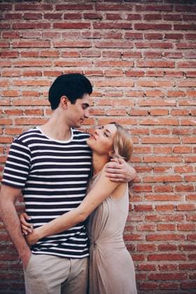 Young cheerful couple in casual clothes having fun during dating outdoors embracing in front of brick wall, Model released Copyright: xRamonxLopezx MR