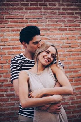 Young cheerful couple in casual clothes having fun during dating outdoors embracing in front of brick wall, Model released Copyright: xRamonxLopezx MR