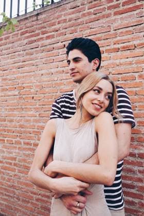 Young cheerful couple in casual clothes having fun during dating outdoors embracing in front of brick wall, Model released Copyright: xRamonxLopezx MR