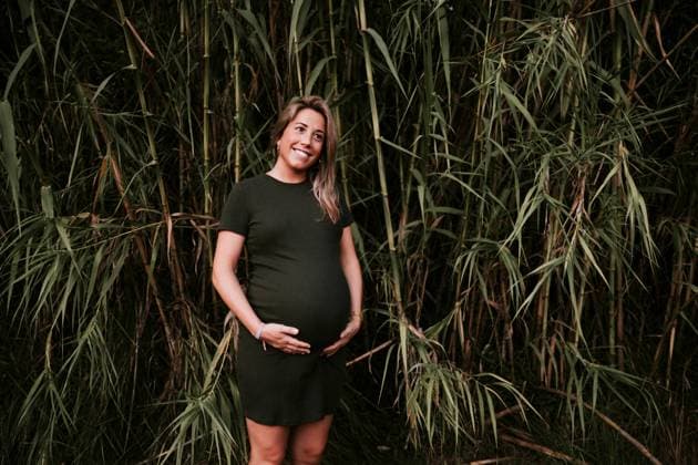 Happy pregnant woman in casual dress stroking belly while standing on green trees wall in sunny summer day with blue sky, Model released Copyright: xSantixMiquelx MR