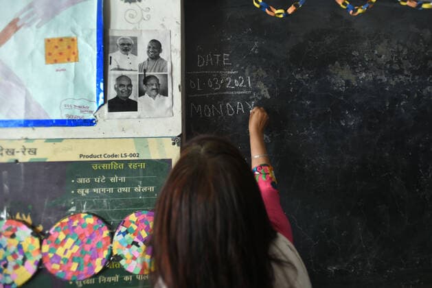 NOIDA, INDIA - MARCH 1: A teacher writing on a blackboard on the first day of school as they reopen after almost a year, at Adarsh primary school sector 12 on March 1, 2021 in Noida, India. Nearly a year after the Centre imposed a nationwide lockdown due to the COVID-19 outbreak, several states and UTs have decided to reopen schools and colleges from March 1. As the deadly virus cases are now steadily dropping, the offline classes are going to resume in states such as Bihar, Meghalaya, Jammu and Kashmir, Haryana, among others. (Photo by Sunil Ghosh Hindustan Times) Primary Schools Reopen For The First Time Since Lockdown Due To Covid-19