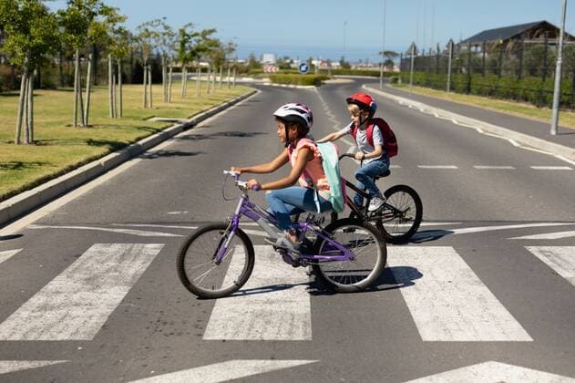Schoolgirls crossing the road with bicycles Side view of a Caucasian and an African American schoolgirl, both wearing cycling helmets and riding bicycles, crossing the road on a pedestrian crossing, on their way to elementary school on a sunny day, model released, , property released, Cape Town, South Africa, 01.12.2019, 1303693.jpg, people,real people,classmates,friends,freindship,school,elementary school,primary school,communication,learn,learning,safety,road safety,road,street,transport,bicycle,bike,eco friendly,green,riding,helmet,protection,journey,travel,independent,development,awareness,crossing,pedestrian crossing,zebra crossing,community,care,backpack,rucksack,childhood,sunny,summer Child,Girl,Female,Mixed-Race,Boy,Male,Caucasian