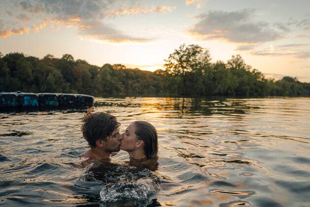 Young couple swimming in lake, kissing at sunset model released Symbolfoto GUSF02323