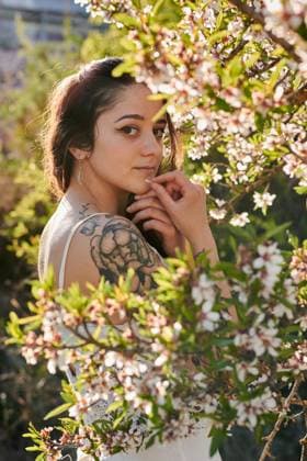 Young female with tattooed arm wearing white dress and standing in flowers of tree looking at camera, Model released, Property released Copyright: xCristianxBlazquezx MR