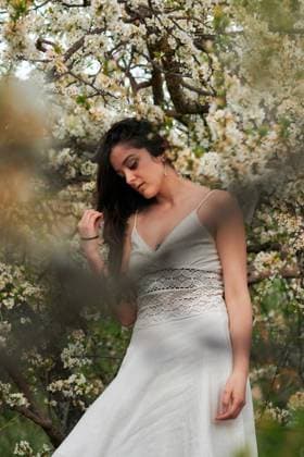 Young female with tattooed arm wearing white dress and standing in flowers of tree looking down, Model released, Property released Copyright: xCristianxBlazquezx MR
