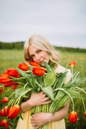 Content female in dress standing with bunch of red tulip flowers in meadow in summer CamilleGirard_GirlWithTulips_17.jpg Copyright: xCamillexGirardx Model Released