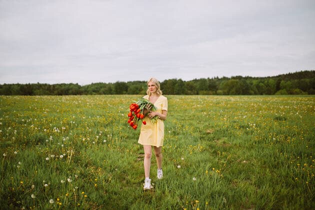 Content female in dress standing with bunch of red tulip flowers in meadow in summer and looking away CamilleGirard_GirlWithTulips_29.jpg Copyright: xCamillexGirardx Model Released