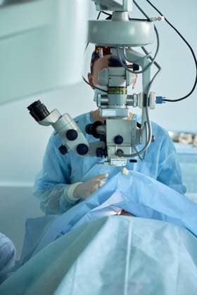 Adult female doctor in sterile mask and ornamental medical cap looking through surgical microscope against crop coworker in hospital, Model released SergeyMironov_Surgery_4.jpg Copyright: xSergeyxMironovx MR