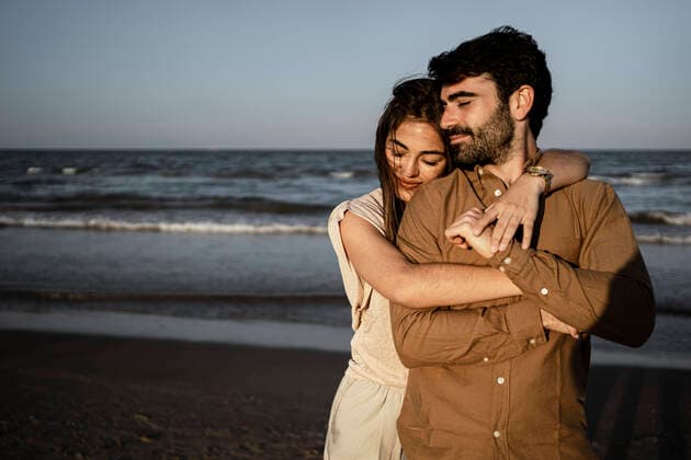 Smiling girlfriend embracing boyfriend from behind at beach model released Symbolfoto RCPF01217
