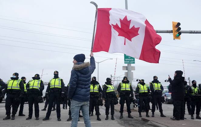 February 12, 2022, Windsor, ON, CANADA: A supporter waves a Canadian flag on a hockey stick as police officers enforce an injunction against their demonstration, which has blocked traffic across the Ambassador Bridge by protesters against COVID-19 restrictions, in Windsor, Ont., Saturday, Feb. 12, 2022. Windsor CANADA - ZUMAc35_ 20220212_zaf_c35_115 Copyright: xNathanxDenettex