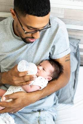 Father bottle-feeding his newborn baby in bed model released, Symbolfoto property released, ERRF01313