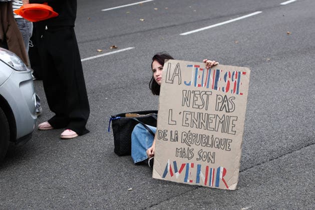 October 2, 2026, Bayonne, Nouvelle Aquitaine, France: A young protester sits on the road to block traffic, holding a cardboard sign reading Youth is not the enemy of the Republic but its future , during a demonstration in Bayonne, southwestern France, on October 2, 2026, against overcrowded classes and a lack of resources. The movement, which began in the Paris region a week ago, has spread across France, with hundreds of high schools blocked. Bayonne France - ZUMAb298 20261002_zsp_b298_003 Copyright: xJulesxBuonx
