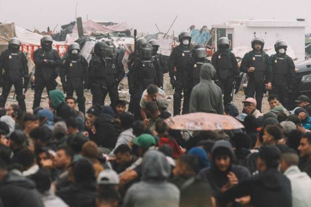 October 4, 2026, Ceuta, Ceuta, Spain: Riot police officers stand in front of hundreds of migrants sitting on the ground during the eviction of the makeshift camp on El Trampolin beach in Ceuta. Spanish National Police began evicting the makeshift camp on El Trampolin beach in Ceuta on October 4, where more than 3,000 migrants, most of them young Moroccan men, were living. Dozens of police vans, armoured vehicles of the Police Intervention Units (UIP), drones and boats took part in the operation. People were taken by bus to the temporary centre at the Tarajal border to be identified, and the authorities plan to clear the beach in phases before October 15. The camp grew after a mass arrival at the end of July 2026 set off a migration and poli - ZUMAs392 20261004_zip_s392_007 Copyright: xFabianxSuspensivox