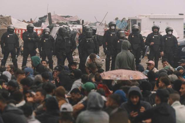 October 4, 2026, Ceuta, Ceuta, Spain: A line of riot police officers stands behind migrants sitting on the ground during the eviction of the makeshift camp on El Trampolin beach in Ceuta. Spanish National Police began evicting the makeshift camp on El Trampolin beach in Ceuta on October 4, where more than 3,000 migrants, most of them young Moroccan men, were living. Dozens of police vans, armoured vehicles of the Police Intervention Units (UIP), drones and boats took part in the operation. People were taken by bus to the temporary centre at the Tarajal border to be identified, and the authorities plan to clear the beach in phases before October 15. The camp grew after a mass arrival at the end of July 2026 set off a migration and political - ZUMAs392 20261004_zip_s392_020 Copyright: xFabianxSuspensivox