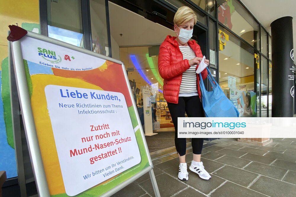 Lockerungen und Maskenpflicht in der Coronavirus Pandemie: Geschaefte in Bayern oeffnen am 27.April wieder. Eine Frau mit Mund-Nasen-Schutz kommt aus einer SaniPlus Apotheke neben einem Hinweis,Aufsteller -Zutritt nur noch mit Mund-Nasen-Schutz gestattet. Ladengeschaeft ,Filiale,Eingang,