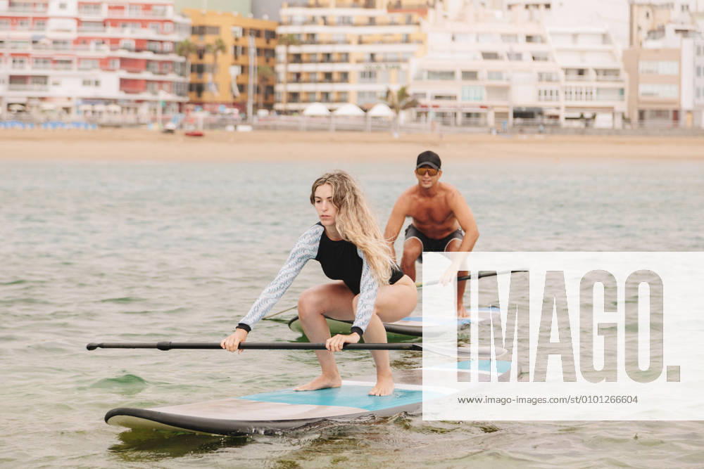 IMAGO Creative, Jahreszeit Sommer, Sommer in der Stadt Young woman practicing paddleboarding with instructor on sea model released Symbolfoto MRRF00033