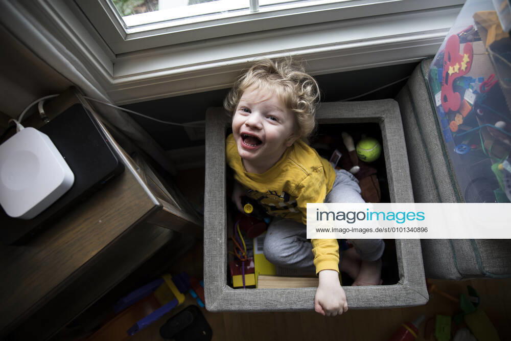 IMAGO Creative: Jahreszeit Winter, Fantasievoll drinnen spielen Laughing Boy Sits in Toy Box Next to Storage Bins Looks Up at Camera Easton, MD, United States CR_EMJA200506A-357579-01,model released, Symbolfoto