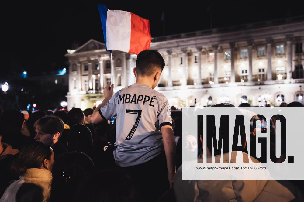 French Football Team Fans Greet The Players On The Place De La Concorde In Paris A child supporter of the French football team wearing an Mbappe jersey sits on his father s shoulders waves a French flag in the middle of the crowd gathered on the Place de la Concorde to welcome the players present on the balcony of the hotel de Crillon after their return from Qatar after their defeat against Argentina in the World Cup final, in Paris, on December 19, 2022. Paris France