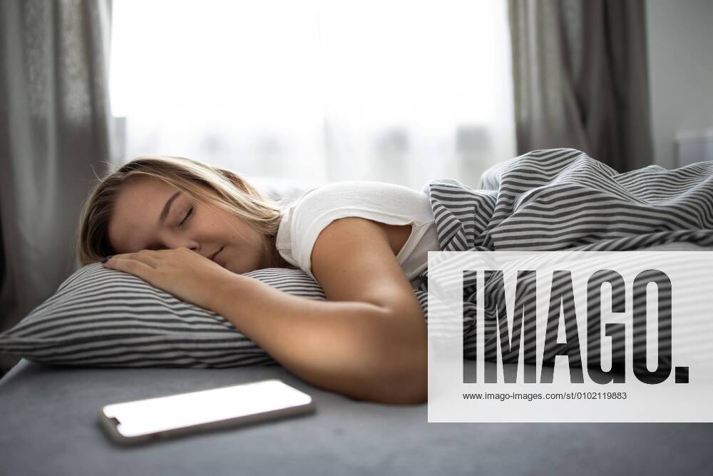 Pretty, young woman sleeping in her bed with her cell phone close to her. Smartphone in Bed Mobile/smartphone Addiction Concept.