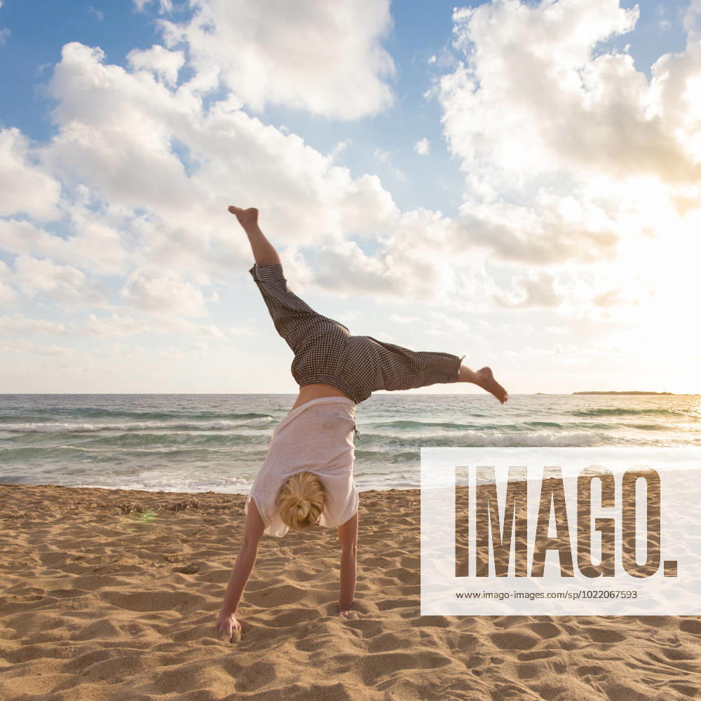 Free Happy Woman Turning Cartwheel Enjoying Sunset on Sandy Beach. Relaxed woman enjoying sun, freedom and life turning cartwheel on beautiful beach in sunset. Young lady feeling free, relaxed and happy. Vacations, freedom, happiness, enjoyment and well being. (License=RF) 10958441