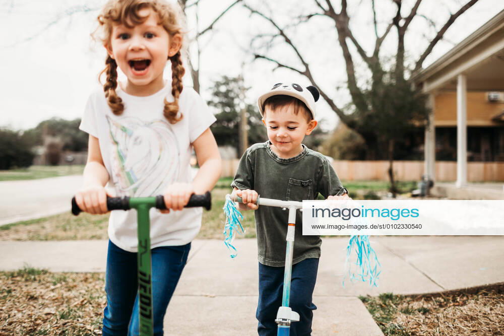 Young sister and brother riding scooters outside in front yard Fort Worth, TX, United States CR_TAHI200701-413913-01 ,model released, Symbolfoto