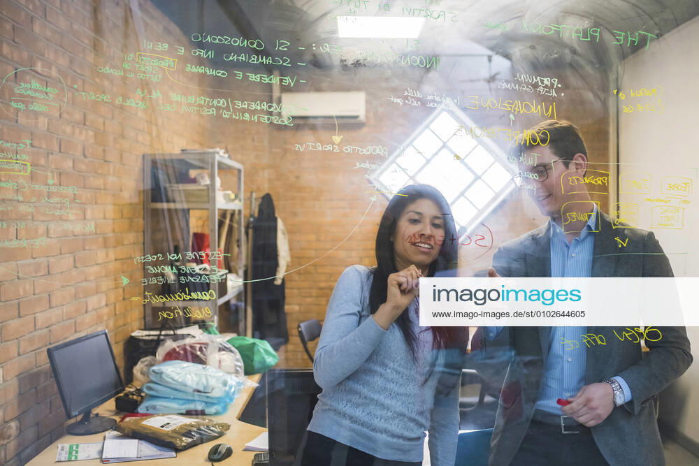 Businessman and woman brainstorming taking notes on glass pane in office model released Symbolfoto property released MEUF00848