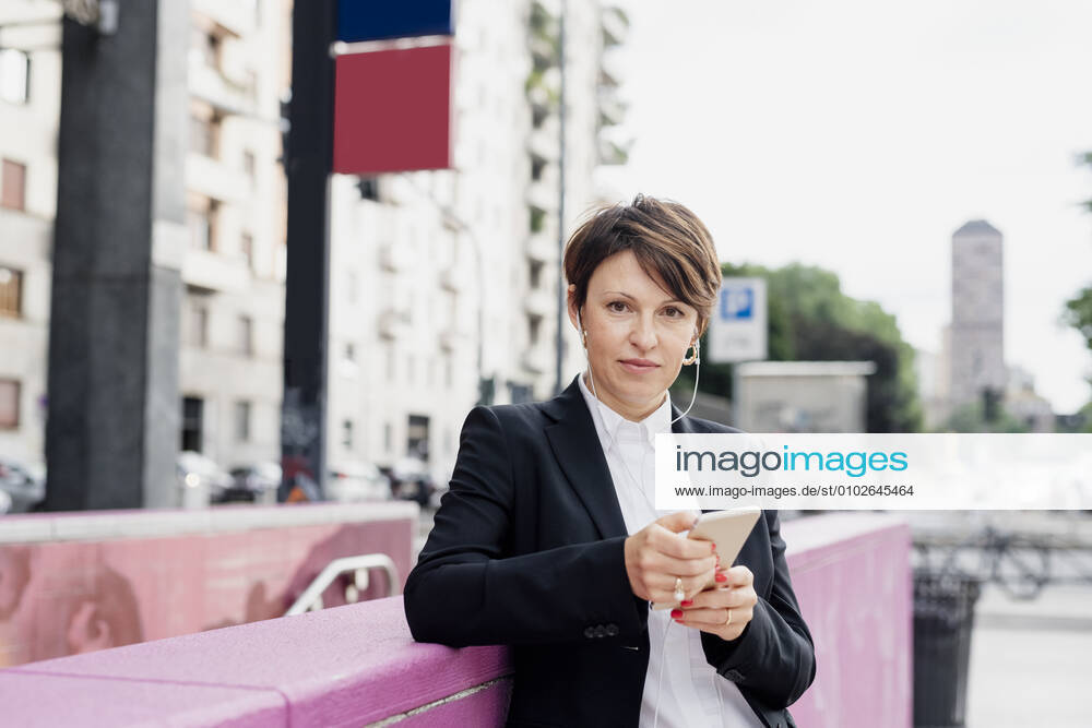 Female professional using smart phone while standing by retaining wall in city model released Symbolfoto MEUF01215