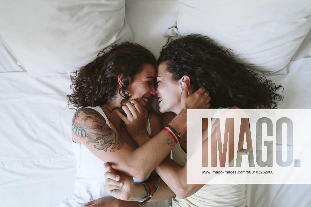 Happy lesbian couple romancing while lying on bed at home model released Symbolfoto property released EBBF00456